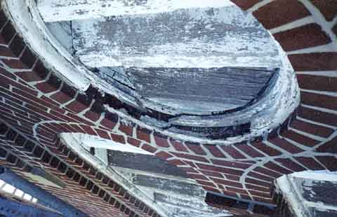 Photograph of rotten wood on round window frame aside the bell tower.